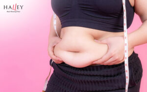 Woman pinching her belly fat rolls with a measuring tape.
