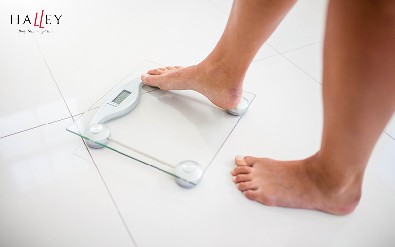 Halley Body Slimming Clinic | Banana Rolls: Why They Form and Non-Surgical Ways to Reduce Them Person stepping on a scale to check their weight.
