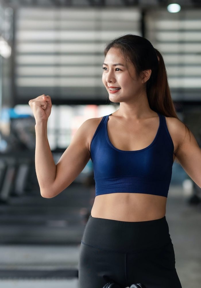 Woman fit and healthy raises hands and show muscles feel proud about her achievement in gym